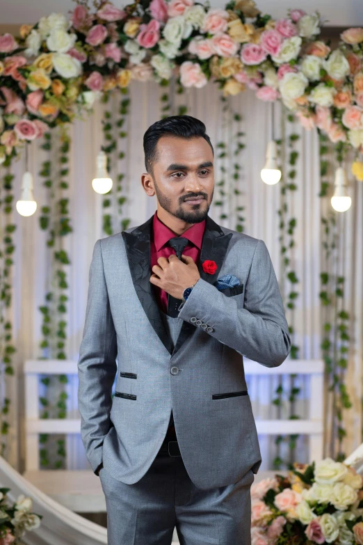 a man in grey suit and tie standing next to flower decoration