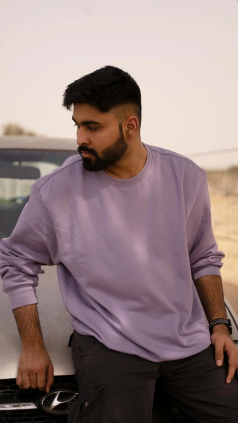 a man in a purple shirt leaning against a car