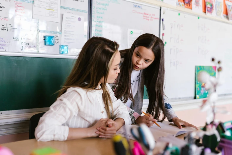 three girls sitting at a table and writing on some papers