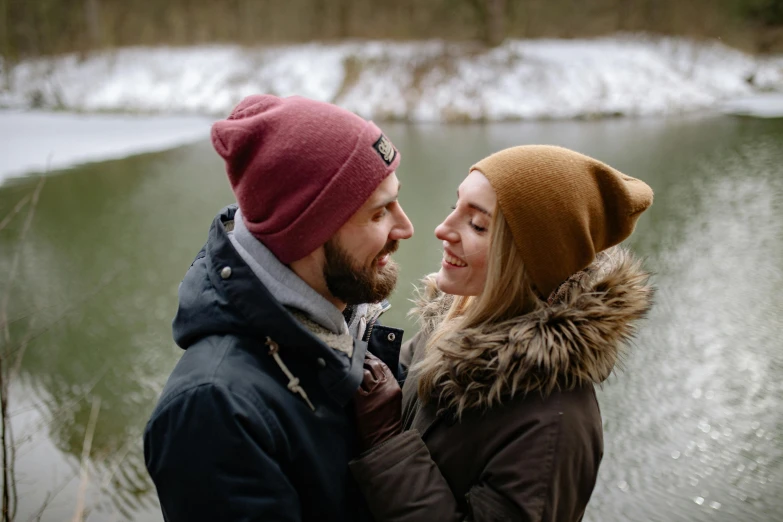 a man and woman standing near a pond, one holding the other to her chest