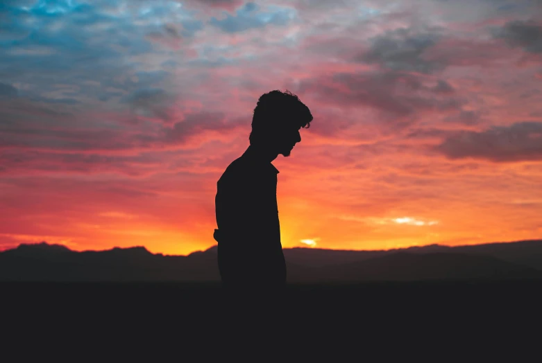 a man looks at a colorful sky while the sun sets