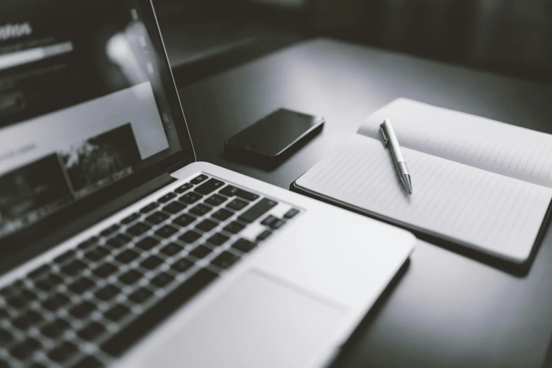 a desk with a laptop, phone and tablet with a book on top