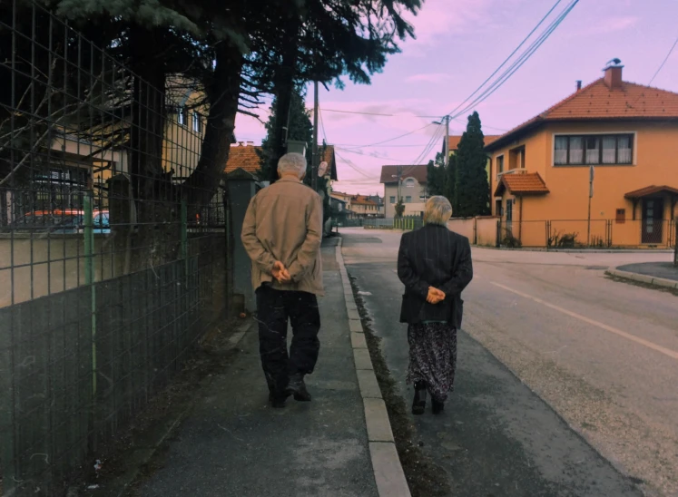 two people walking down a street near a fence