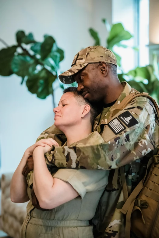 the military couple is hugging in front of the plant