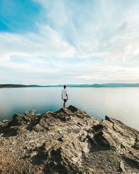 a man is standing on the edge of a rock near water