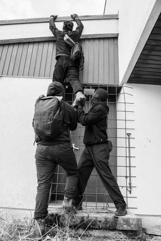 three men, one carrying a backpack and one hanging on the fence