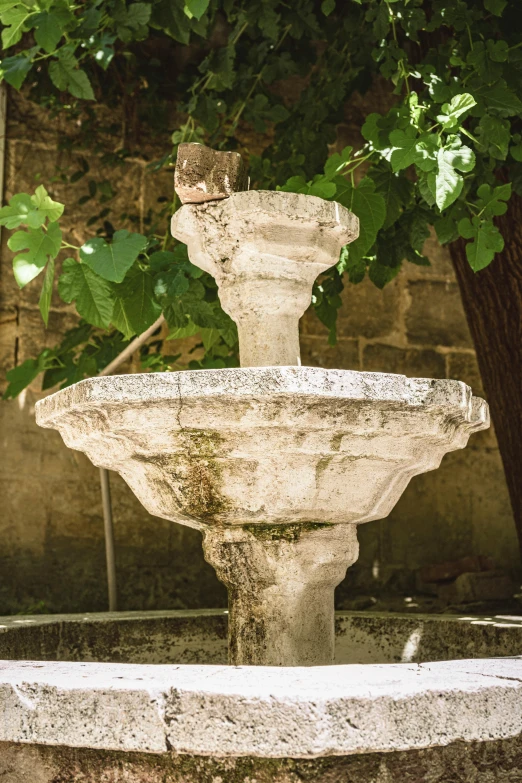 a concrete fountain near a brick wall and trees