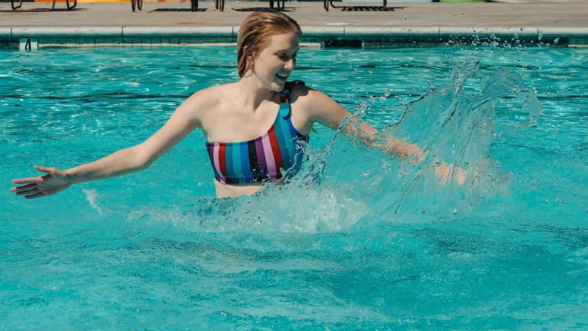 girl in bikini splashes into pool on  summer day