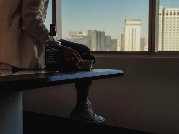 a person standing at a window sill with an alcoholic drink