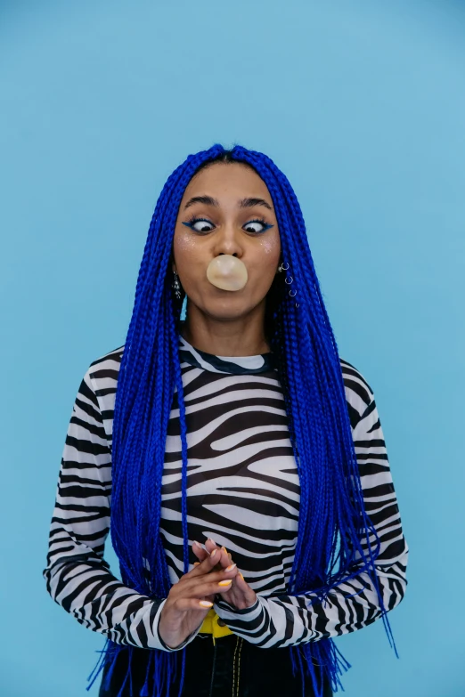 a woman with blue dreadlocks and a  shirt blowing out a bubble