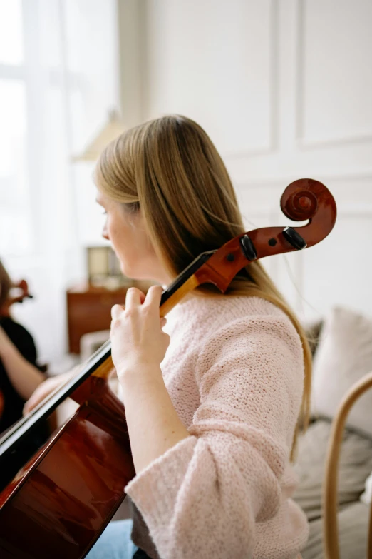 woman holding a cello, with another woman sitting next to her in the background