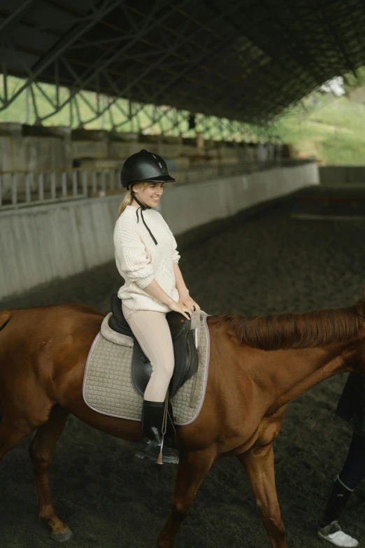 a young lady wearing all white riding on the back of a brown horse