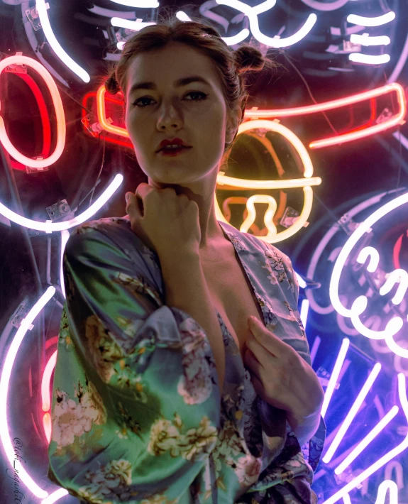 the woman wearing a robe stands by some neon signs