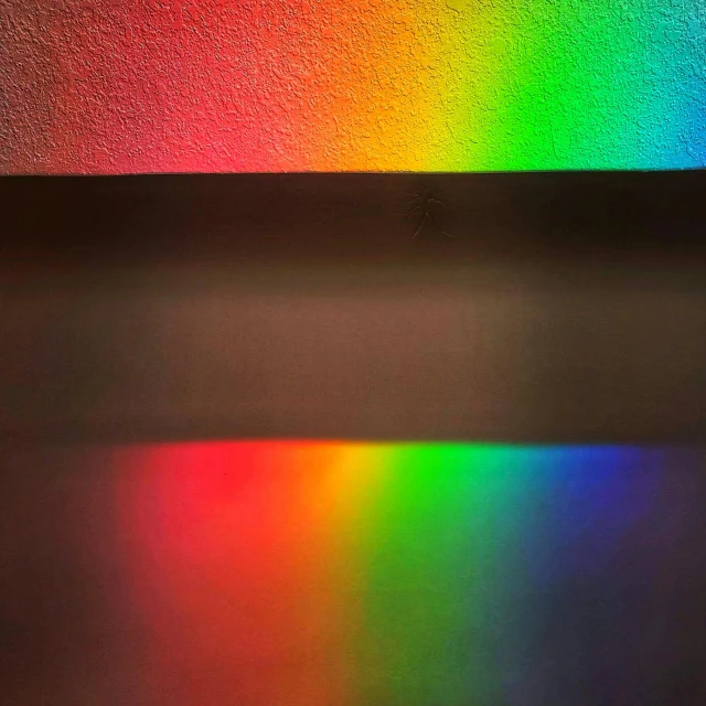 a black wall with a color light reflecting in the middle of it