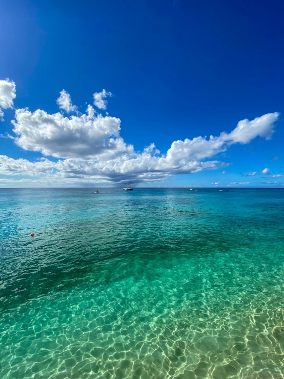 clear blue ocean with clouds, blue sky and a boat in the distance