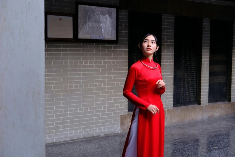 a woman standing on the sidewalk looking up with a red dress on