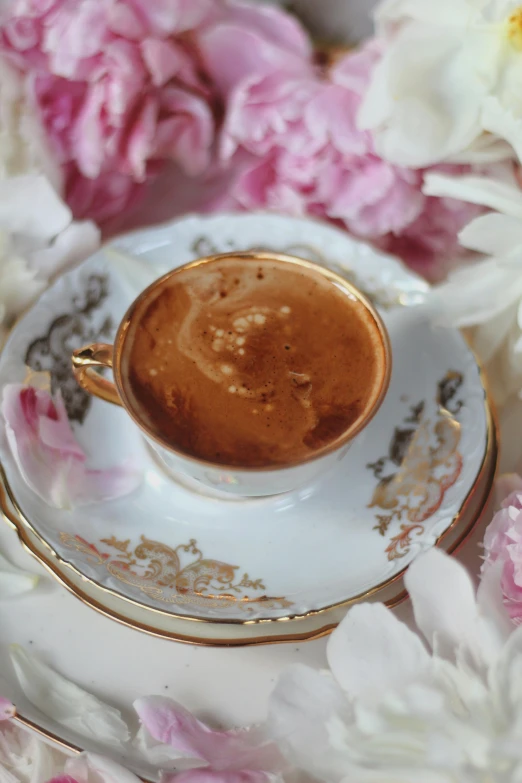 a cup of chocolate sits on an elegant saucer surrounded by pink roses