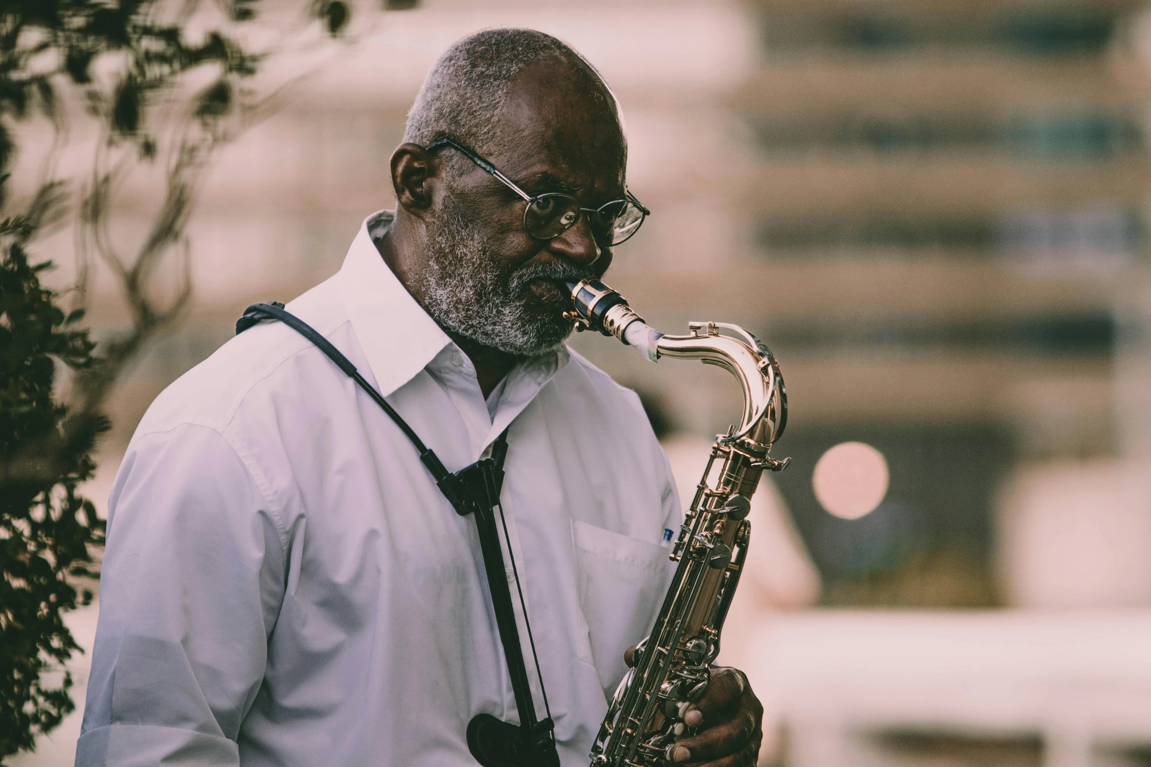 man in white shirt playing saxophone outdoors