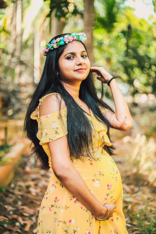 pregnant woman wearing floral headpiece stands in forest