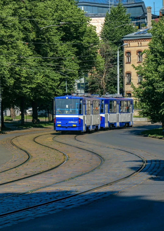 a blue train is rolling down the tracks near some buildings