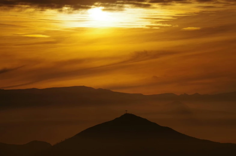 the sun rises over a mountain with a cross atop it