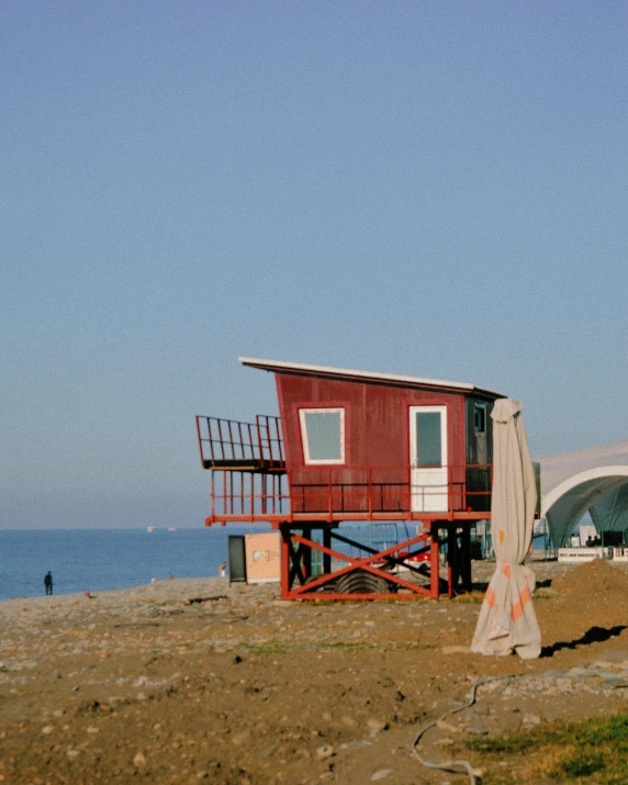 an old beach shack is red on the sand by the water