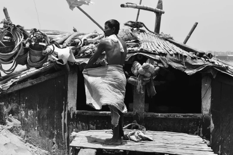 man standing outside of shack that is covered with items