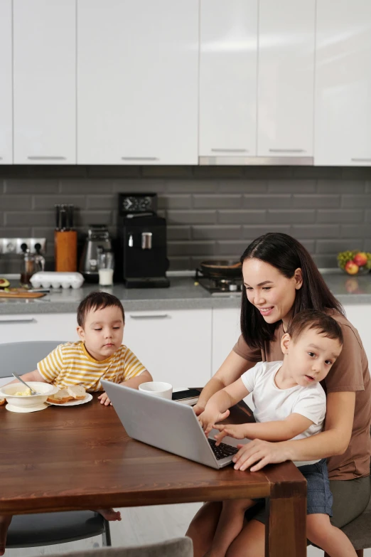 a woman sitting at a kitchen table working on her laptop