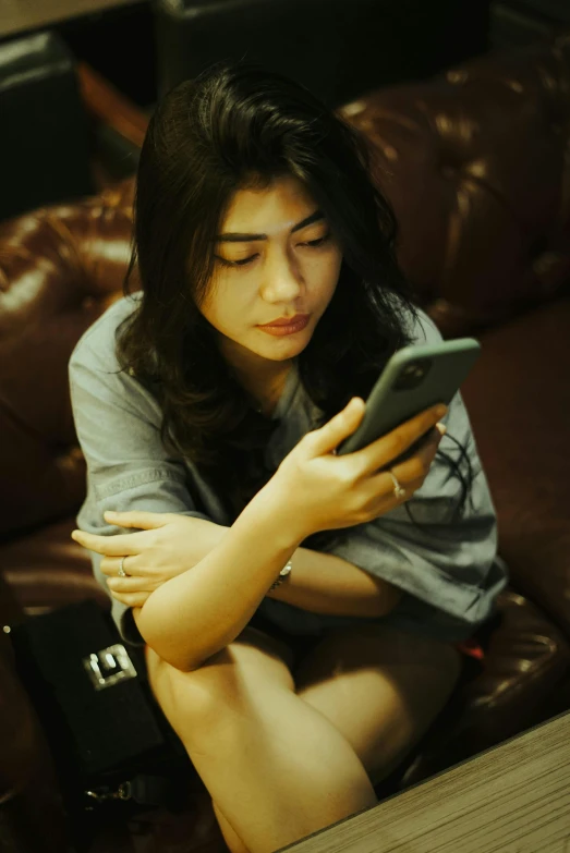 a woman in a gray shirt and jeans is holding a cell phone