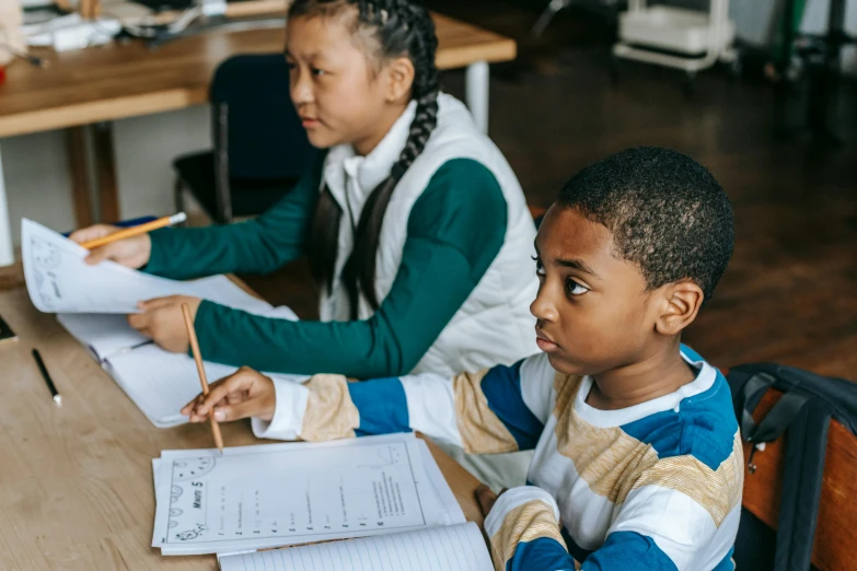 children sitting at a desk studying while others stand in the background