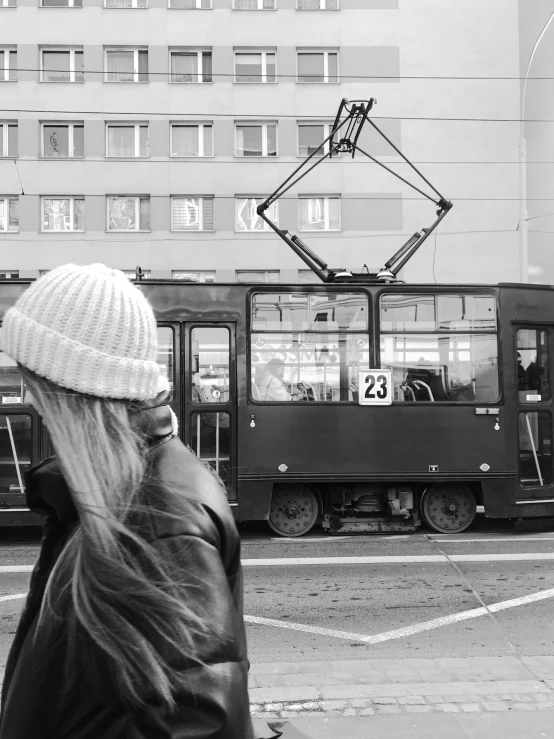 a woman in a hat on a street corner near an old tram
