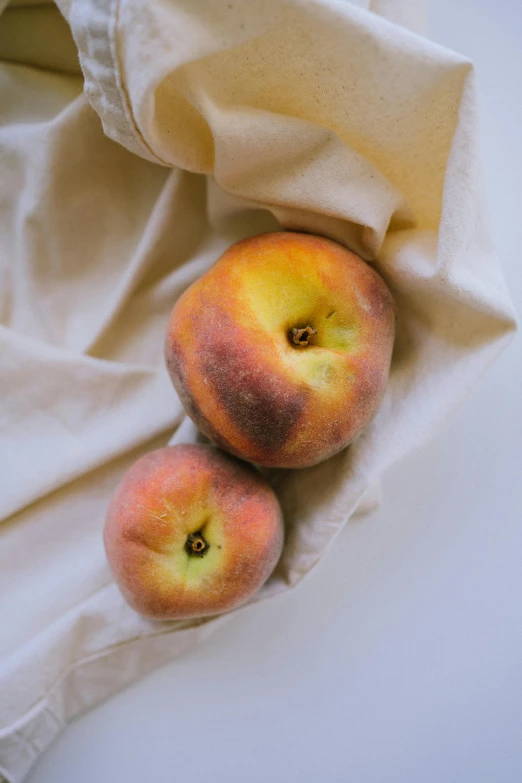 two peaches with the tops cut off laying on a white cloth