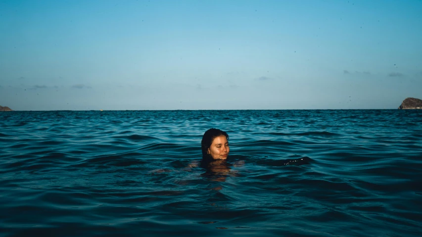 a woman swimming in the blue water near some islands