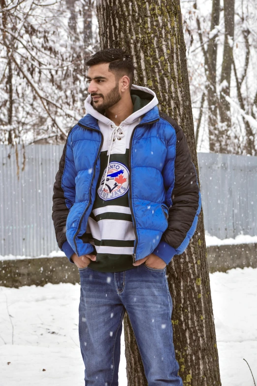 a man in jeans and jacket leaning against a tree