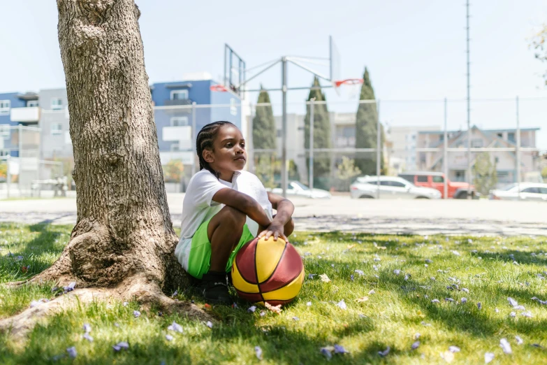 the little girl is holding onto the basketball ball near a tree