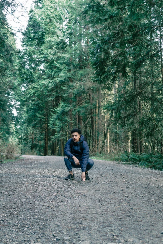 a woman kneeling down on a gravel road near some trees