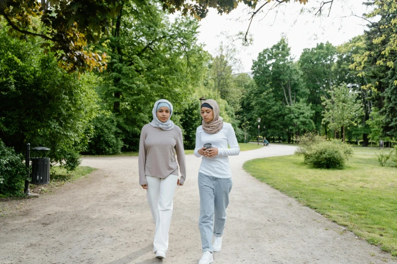 two women walking down a dirt road in the middle of a park