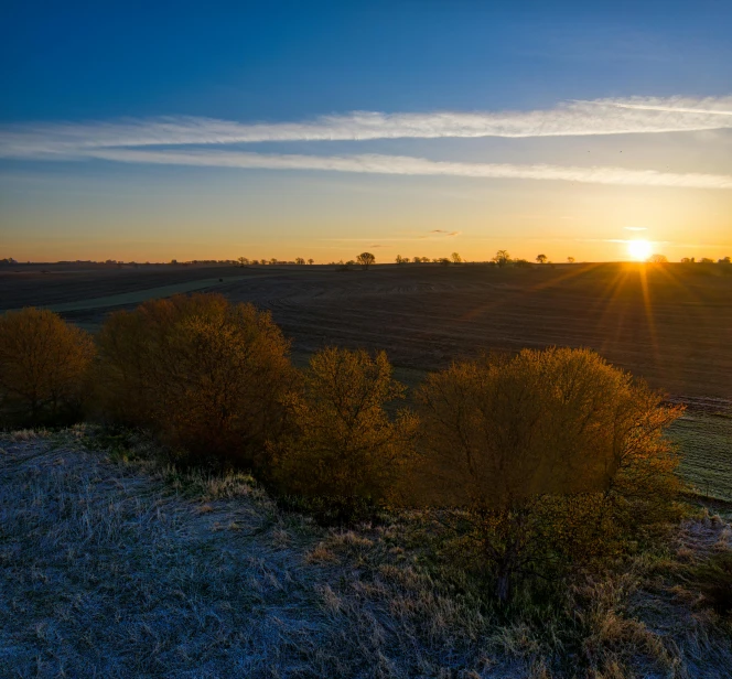 the sun rising over the land next to the field