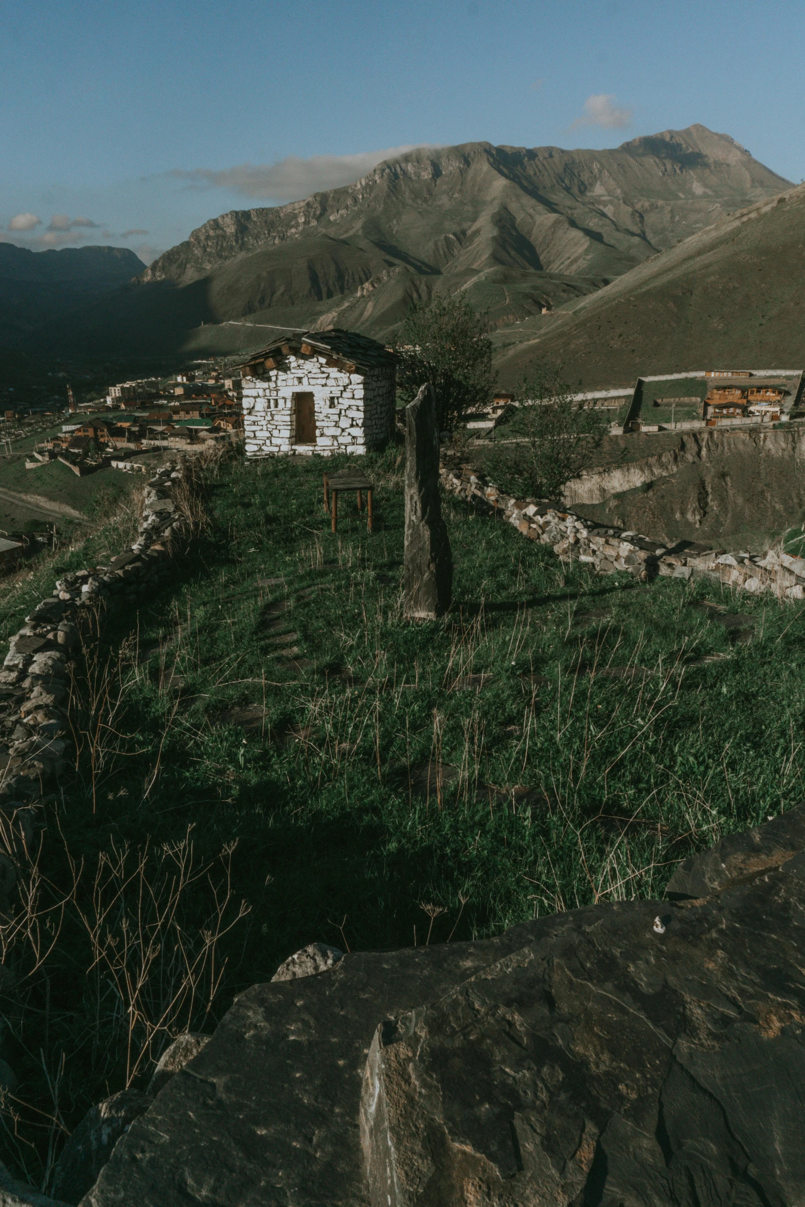 an old building sitting in a field with mountains behind it