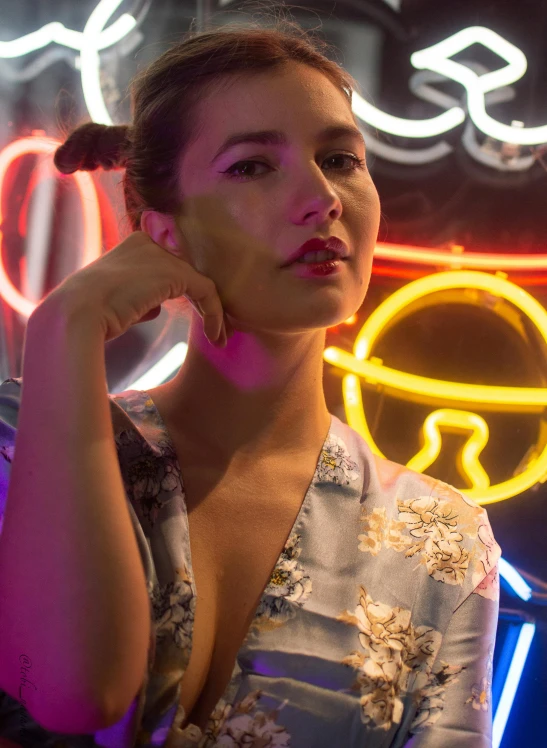 a woman in a dress stands against a neon light