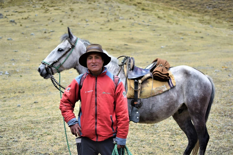 a man wearing red jacket and hat standing with a horse