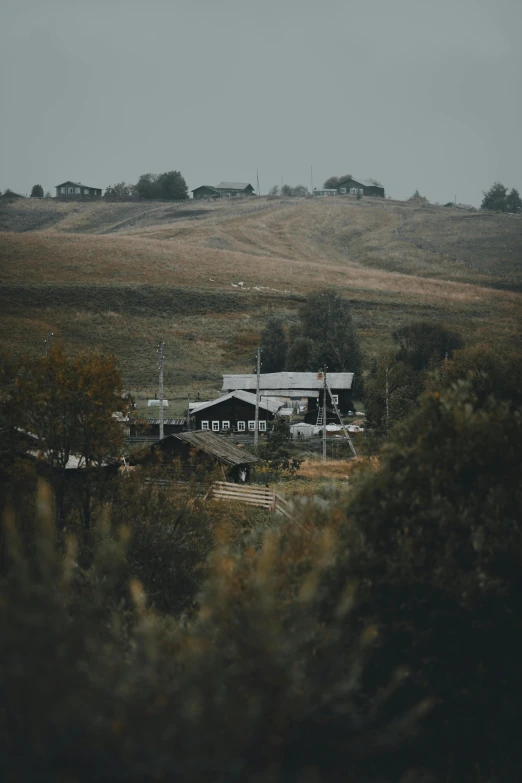 an old farm is surrounded by trees on a hill