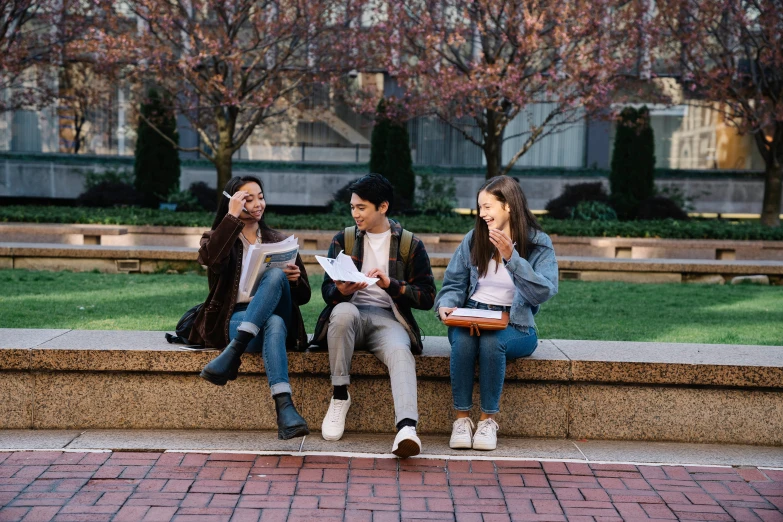 a group of three people sitting on the edge of a wall with books