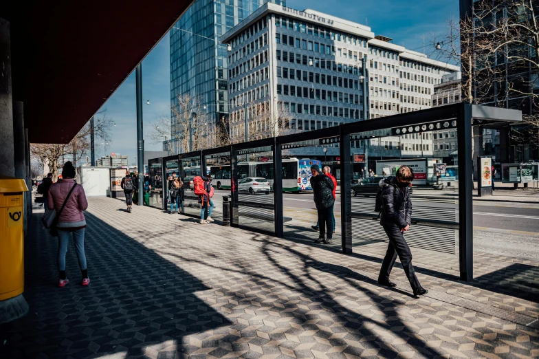 people are walking down the sidewalk while waiting for a bus