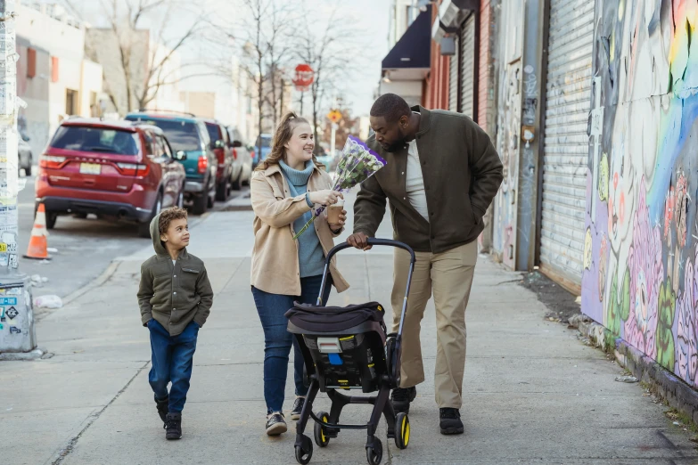 a man holds flowers in front of two children as they stroll down a sidewalk