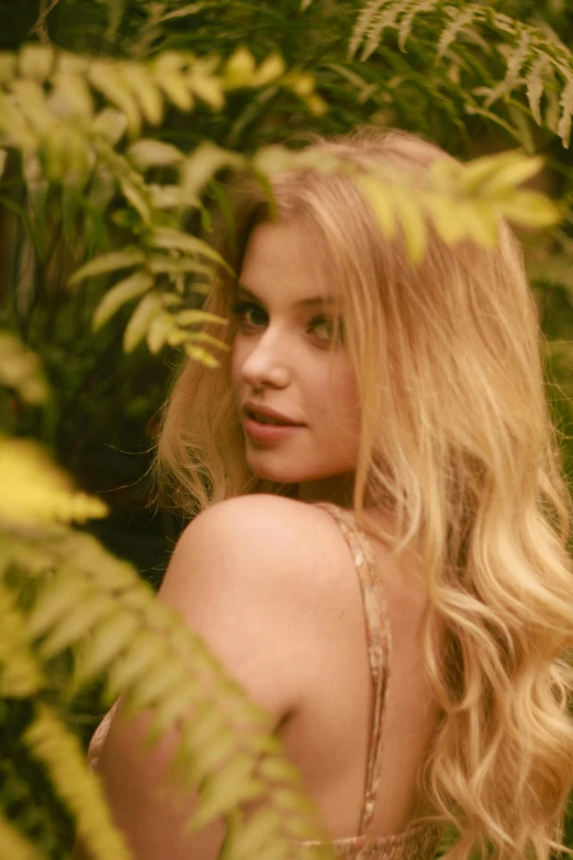 a woman with blonde hair and brown eyes looking out from behind the trees