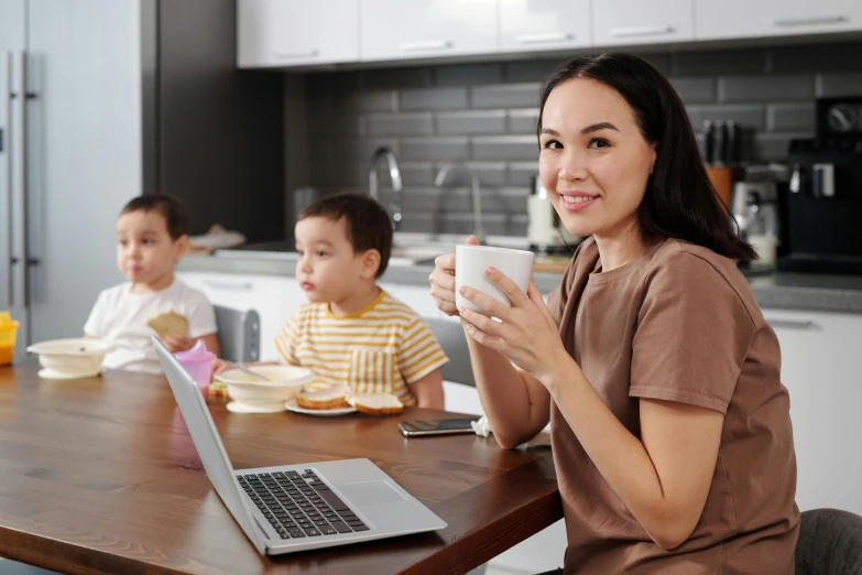 a woman drinking tea sitting at a wooden table while looking into the camera