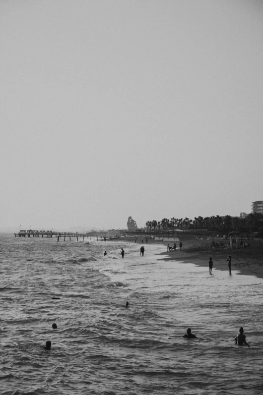 several people swim on the beach next to a pier