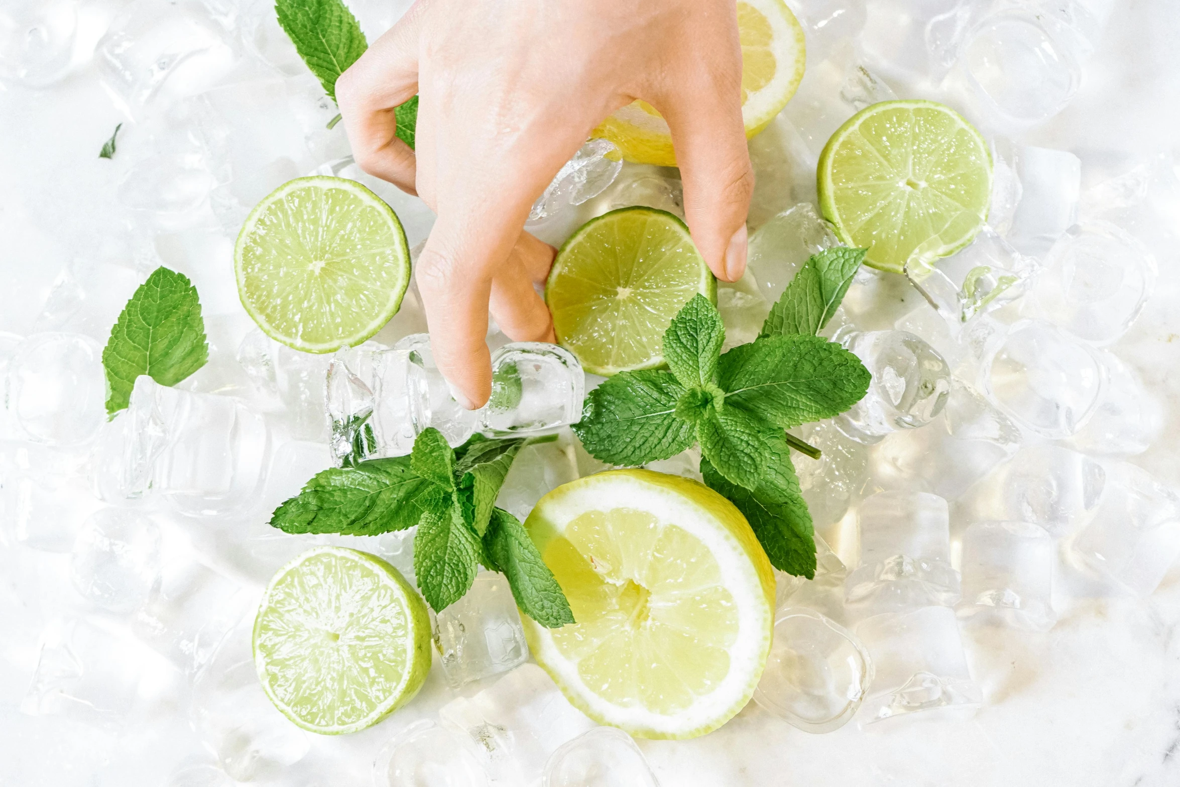 two hands holding a cocktail glass with ice and lime slices on ice