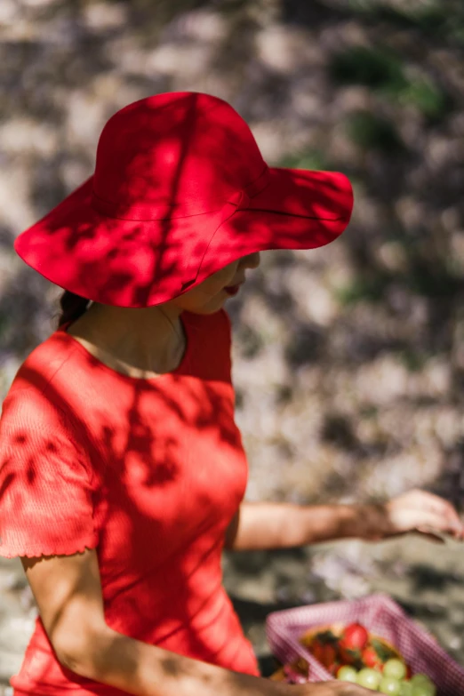 a woman with a red hat holds a basket and looks at the ground